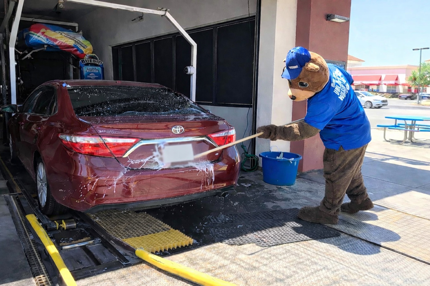 Bubba's mascot hand-prepping a red Toyota Camry at the wash entrance
