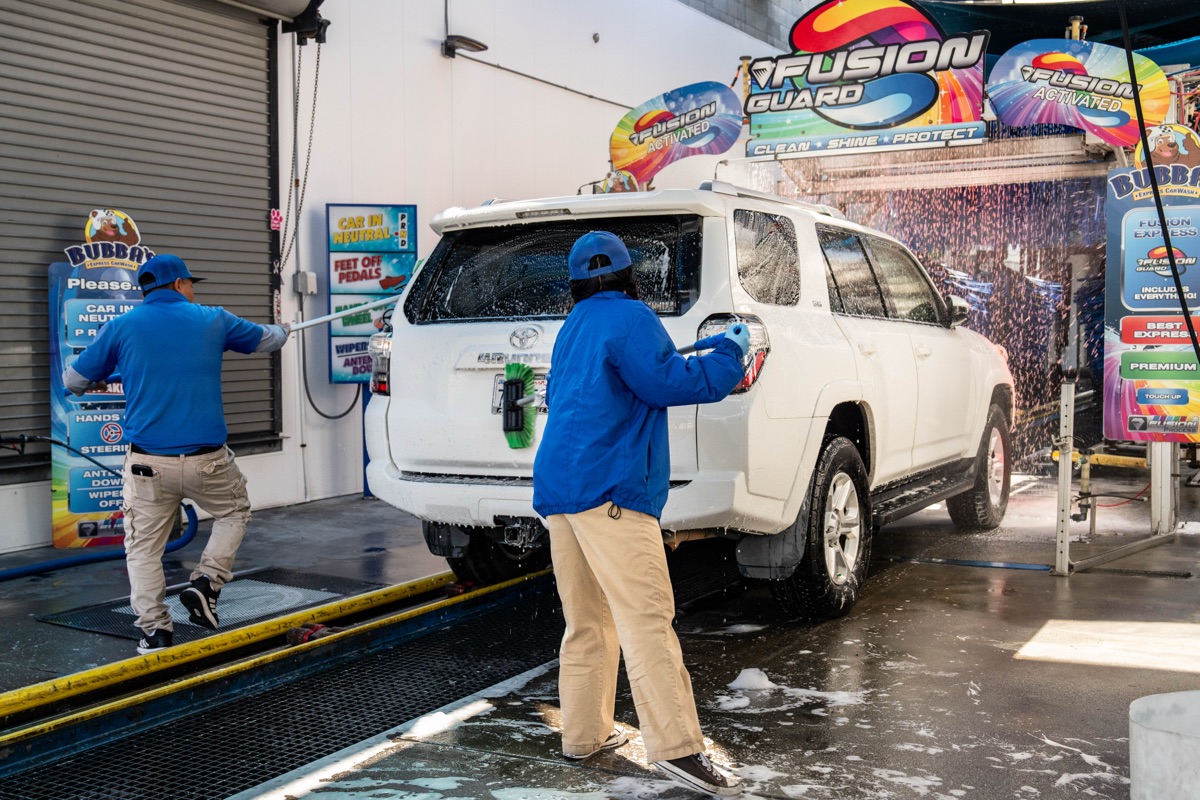 Two Bubba's team members hand prepping the rear of a vehicle before it enters the wash tunnel