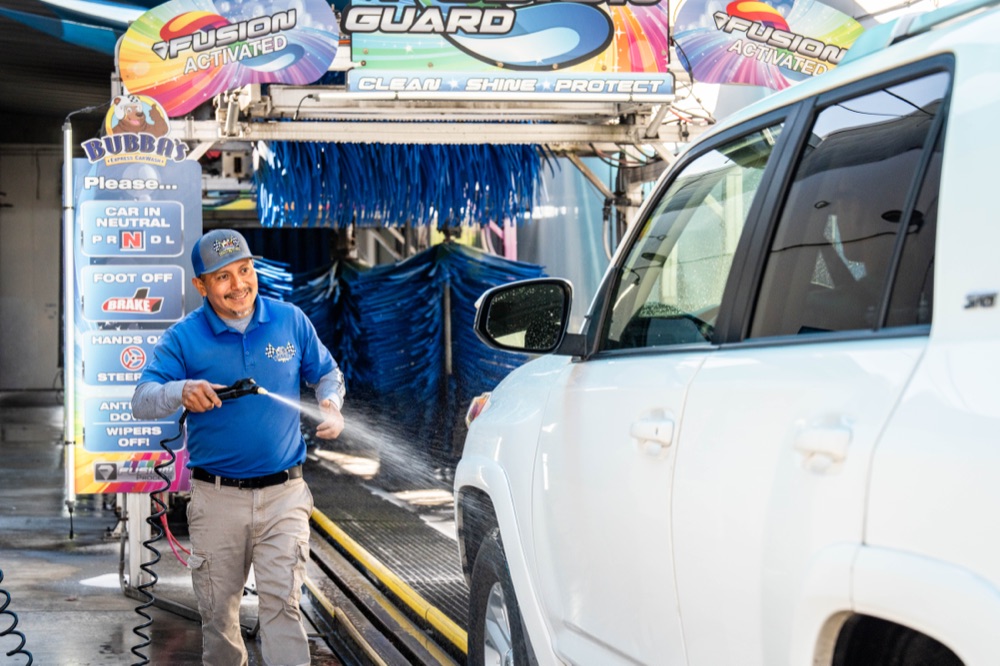 Smiling Bubba's team member hand prepping a vehicle at the tunnel entrance