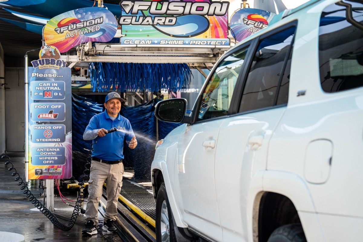 Bubba's team member hand prepping a vehicle at the tunnel entrance with Fusion Guard signage